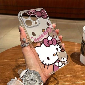 Puede incluir: Funda transparente para tel&eacute;fono con un dise&ntilde;o de Hello Kitty, con un lazo rosa y un peque&ntilde;o osito de peluche. La funda tiene las palabras "Hello Kitty" en rosa. La funda se sostiene en una mano.