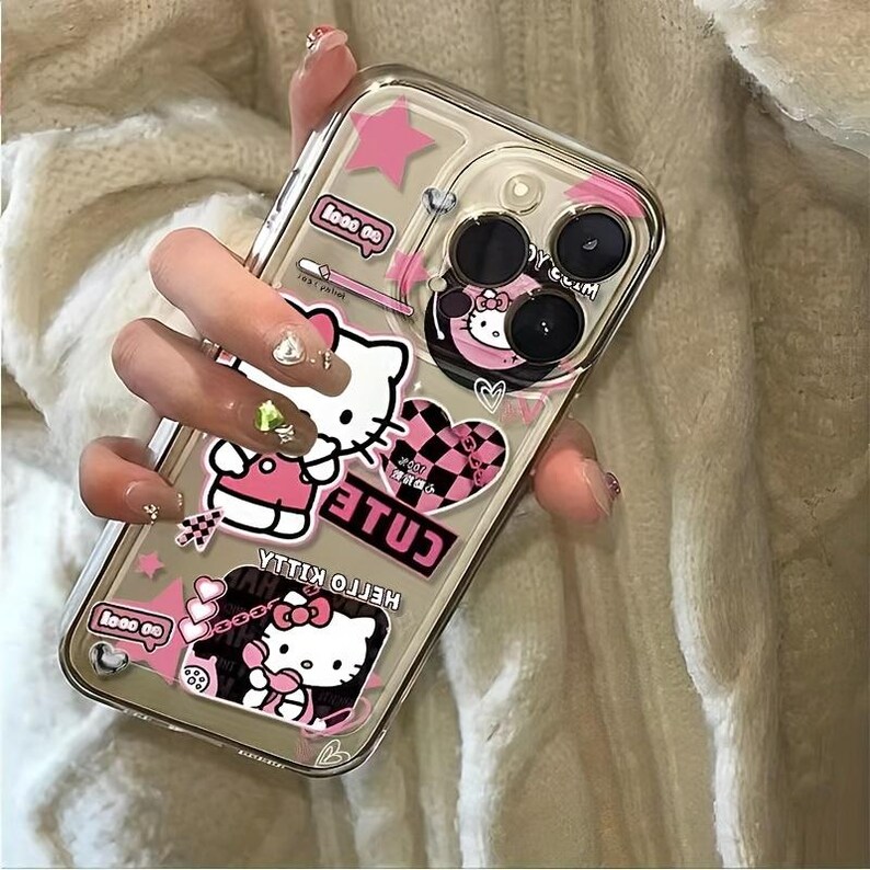 K&ouml;nnte beinhalten: Transparente Handyh&uuml;lle mit rosa und schwarzen Hello Kitty Aufklebern, Sternen und Herzen. Die H&uuml;lle hat ein transparentes Design mit gl&auml;nzendem Finish, das die Kamera und die Tasten des Telefons zeigt. Die Aufkleber enthalten die W&ouml;rter "cute" und "Hello Kitty".