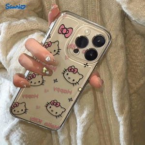 May include: Clear phone case featuring a repeating pattern of Hello Kitty faces with pink bows and the word "Happy" in pink. The case has a pink bow at the top and is designed for a smartphone with multiple camera lenses.