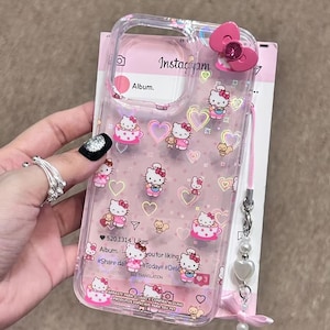May include: Clear phone case featuring Hello Kitty designs, pink hearts, and a pink bow. The case has a pink strap with a pearl and heart charm. The case has the text "Insta&ccedil;yam" and "Album."