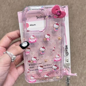 May include: Clear phone case with a pink bow and Hello Kitty graphics. The case features a pink lanyard with pearl accents and text that reads "Instagram" and "Album."