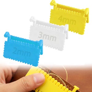 May include: Three plastic stitch spacing gauges in blue, white, and yellow, labeled 2mm, 3mm, and 4mm. A hand is using a yellow gauge to measure the stitch spacing on a leather item. The gauges have a notched edge.