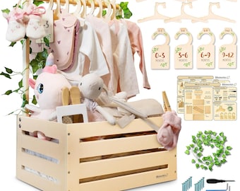 May include: A light-coloured wooden baby clothing rack with a storage crate base, featuring hanging baby clothes, wooden hangers, size dividers labelled 0-3, 3-6, 6-9, and 9-12 months, a plush unicorn, a plush rabbit, artificial ivy vines, and assembly hardware.
