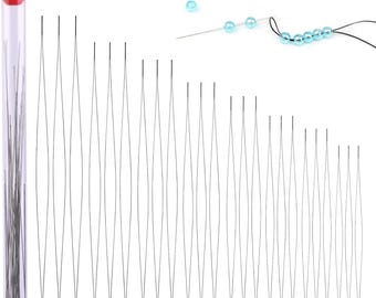 May include: A selection of long, thin beading needles in a clear plastic tube with a red cap. Several loose needles are also visible, along with a needle threaded with black thread and strung with light blue beads. The needles are for jewellery making.