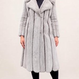May include: A long, light gray fur coat with vertical dark stripes. The coat has a wide collar and long sleeves. The person is wearing black pants and black pointed-toe heels. The coat appears to be knee-length.