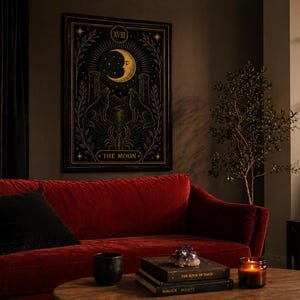 May include: A framed tarot card print featuring a crescent moon, two wolves, and the text "THE MOON." The artwork is in a dark color palette with gold and purple accents. The print hangs above a red velvet sofa with a black pillow.