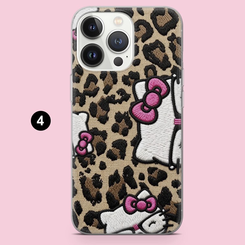 Puede incluir: Una funda para smartphone con estampado de leopardo en tonos beige y marr&oacute;n, decorada con personajes de gatos blancos bordados que llevan lazos de color rosa brillante. La funda tiene un recorte para una c&aacute;mara triple y el n&uacute;mero cuatro.