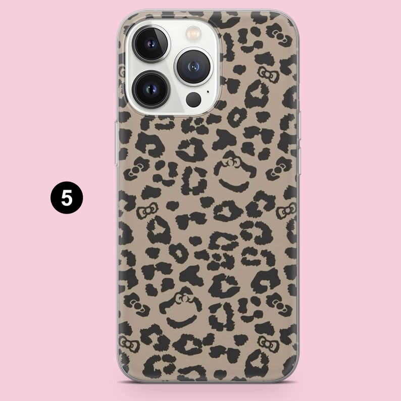 Puede incluir: Una funda para smartphone con fondo beige y estampado de leopardo negro. El patr&oacute;n incorpora peque&ntilde;os lazos negros integrados en las manchas. La funda tiene un recorte para un sistema de c&aacute;mara de tres lentes en la parte superior izquierda.