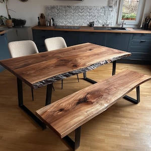 May include: A live edge walnut wood dining table and matching bench set featuring natural wood grain patterns and dark brown tones. Both pieces are supported by black metal U-shaped legs, providing a sturdy base for the solid wood surfaces.