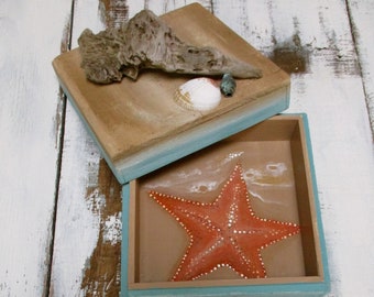 May include: A wooden box with a blue and brown painted finish. The box is open and reveals a painted orange starfish on a tan background.