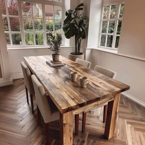 May include: A reclaimed wood dining table with a natural finish, accompanied by four upholstered chairs. Two mugs are placed on the table. The room features large windows and potted plants, creating a cosy atmosphere.