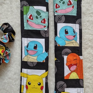 May include: Two black seatbelt covers featuring colorful cartoon characters. Each cover has a repeating pattern of the characters Bulbasaur, Squirtle, Charmander, and Pikachu. The covers are made of fabric and are designed to protect seatbelts.