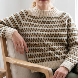 May include: Cream-colored sweater with a geometric pattern in shades of green and brown. The sweater has a ribbed neckline, cuffs, and hem. The design features a repeating diamond pattern. The sleeves are long and the sweater is a crew neck style.