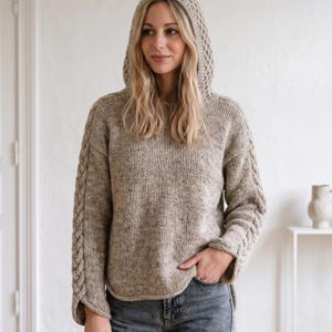 Op de afbeelding: Een beige hoodie met kabelgebreide details op de mouwen en capuchon. De trui heeft een relaxte pasvorm en is gemaakt van een getextureerde gebreide stof. De mouwen hebben een split manchet ontwerp.