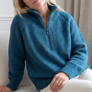 May include: A teal blue long-sleeve jumper featuring a ribbed knit texture, a high collar, and a metal zip closure extending from the neckline to the chest. The garment has raglan sleeves and ribbed cuffs, providing a structured fit.
