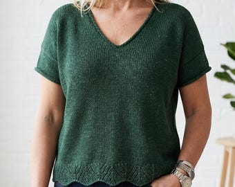 Puede incluir: Una camiseta de punto verde oscuro de manga corta con cuello en V. La parte superior tiene un aspecto texturizado y un dobladillo festoneado. La modelo lleva la camiseta con vaqueros azules. La parte superior es una prenda cómoda y elegante.