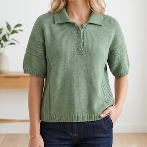 Könnte beinhalten: Ein salbeigrünes Strick-Poloshirt mit kurzen Ärmeln und Kragen. Das Shirt hat eine Knopfleiste mit drei Knöpfen und Rippendetails an den Ärmeln und Seiten. Das Model trägt eine dunkelblaue Jeans.