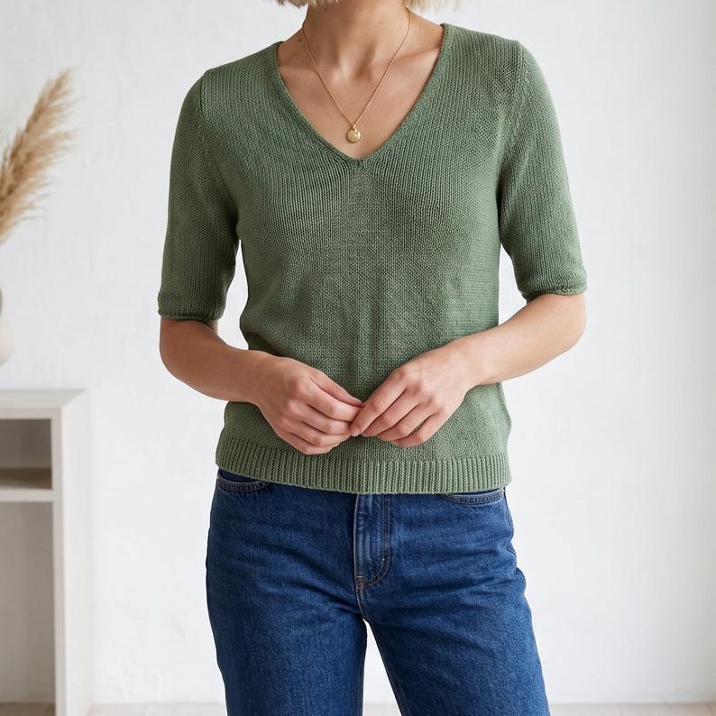 1. Woman wearing a green knitted V-neck short sleeve top with layered necklaces  
2. Close-up of lightweight knit tee showing smooth stockinette texture and neckline  
3. Minimalist summer knit top styled with neutral pants and jewelry  
4. Detail of V-neck shaping on handmade knitted short sleeve sweater  
5. Soft lightweight knitted tee worn casually indoors with modern styling