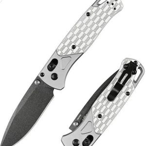 May include: Two folding knives with silver handles and dark gray blades. The handles feature a white checkered pattern with the word "KITH" repeated. One knife is open, the other closed.