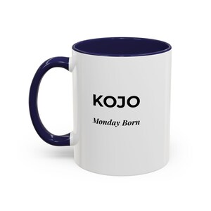 May include: White ceramic mug with a navy blue interior and handle. The mug features the name "KOJO" in bold black letters, with "Monday Born" printed below it in a smaller font. A simple, modern design.