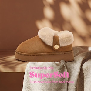 May include: A tan suede slipper with a thick platform sole and a plush cream-colored faux fur collar. A small brown tab with a single light-colored button secures the side. The text DrNatsuStudio SuperSoft Cushioned sole from heel to toe is visible.