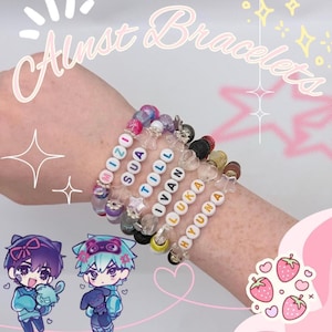 May include: A stack of six beaded bracelets featuring white letter beads spelling MIZI, SUA, TILL, IVAN, LUKA, and HYUNA. The bracelets include colorful round, star-shaped, and textured black beads, with the text Alnst Bracelets visible at the top.