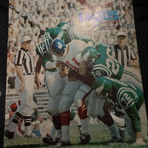 May include: A vintage Eagles Magazine from September 25, 1966, featuring a color photograph of a football game in progress. The cover shows players in green and white uniforms tackling a player in a white jersey, with a referee standing nearby.