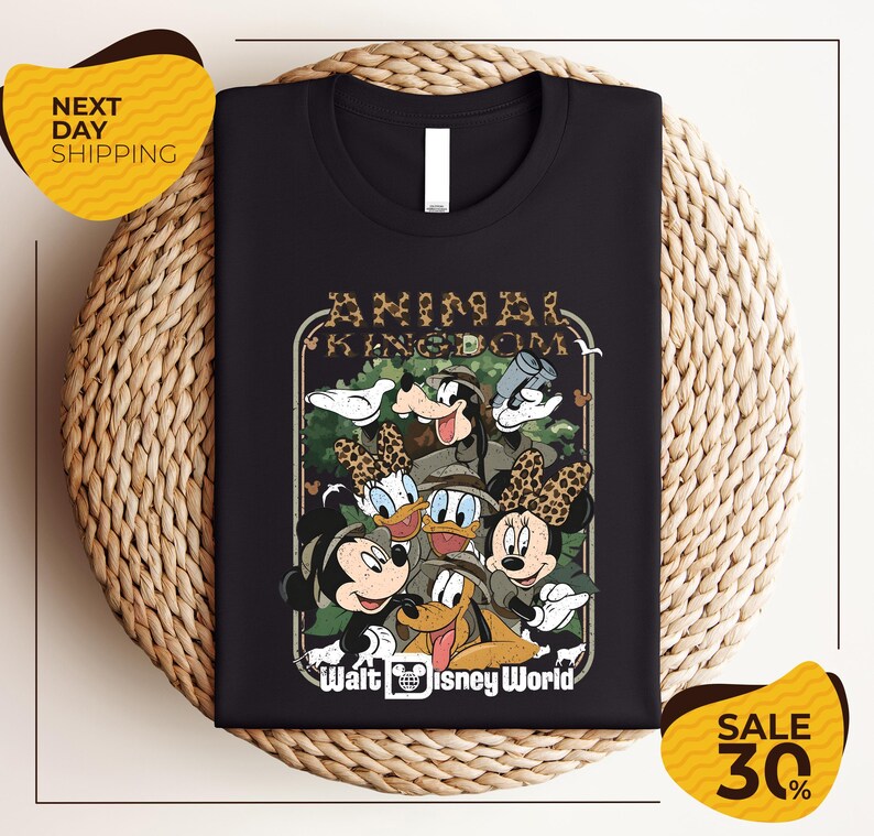 A black t-shirt with a graphic design featuring various Disney characters, including Mickey Mouse, Minnie Mouse, Donald Duck, Goofy, and Pluto, arranged in a circular frame.
