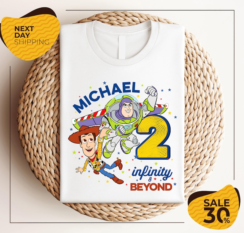 A white t-shirt with a graphic design featuring characters from the Toy Story franchise, specifically Buzz Lightyear and Woody, along with the text "Michael 2 infinity beyond". The t-shirt is displayed on a woven placemat, and there are yellow price tags with text indicating a sale of 30% off.
