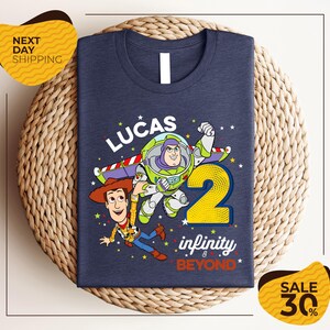 A blue t-shirt with a graphic design featuring Buzz Lightyear and Woody from Toy Story, along with the text "Lucas 2" and " Infinity & Beyond".