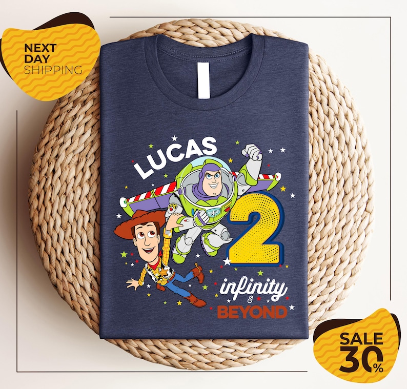 A blue t-shirt with a graphic design featuring Buzz Lightyear and Woody from Toy Story, along with the text "Lucas 2" and " Infinity & Beyond".
