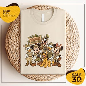 A t-shirt featuring a cartoon illustration of Disney characters dressed in safari attire, including Minnie Mouse, Goofy, Donald Duck, and Pluto, along with a sign that says "Safari Adventure".