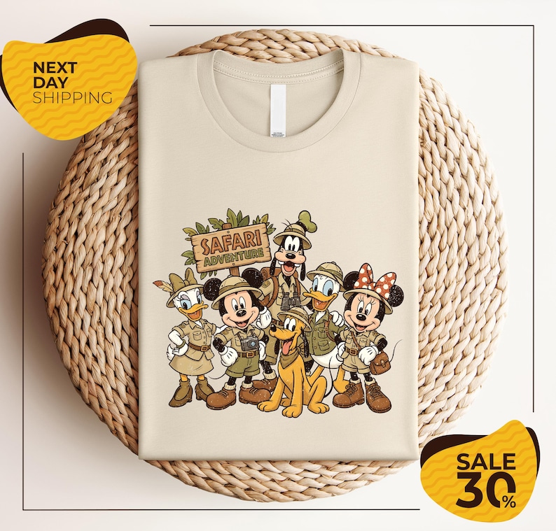 A t-shirt featuring a cartoon illustration of Disney characters dressed in safari attire, including Minnie Mouse, Goofy, Donald Duck, and Pluto, along with a sign that says "Safari Adventure".