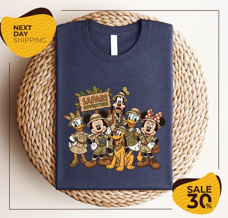 A blue t-shirt with a printed design of Disney characters dressed in safari attire, including Mickey Mouse, Minnie Mouse, Donald Duck, Goofy, and Pluto, along with a safari adventure sign. The t-shirt is displayed on a woven placemat, and there are yellow price tags indicating a sale of 30% off.