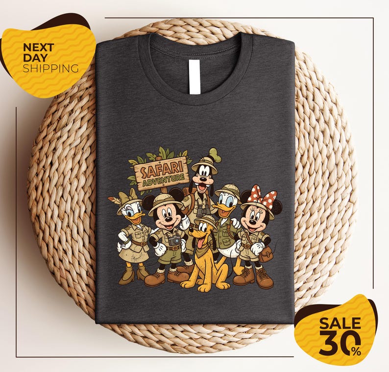 A t-shirt featuring a cartoon illustration of Disney characters dressed in safari attire, including Mickey Mouse, Minnie Mouse, Donald Duck, Goofy, and Pluto, along with a sign that says "Safari Adventure".