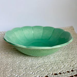 May include: A shallow, round bowl with a scalloped edge and a glossy, light green finish. The bowl features a smooth, curved interior and a distinct petal-like rim design, showcasing a consistent, vibrant green color throughout the entire piece.