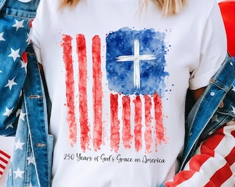 May include: White t-shirt featuring a watercolor design of the American flag with a cross in the blue field. The flag design has red and white stripes and a blue square with a white cross. The text "250 Years of God's Grace on America" is below the flag.