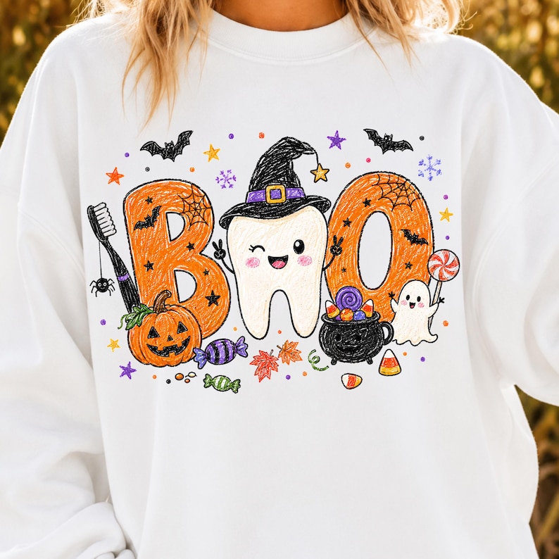 K&ouml;nnte beinhalten: Ein wei&szlig;es Sweatshirt mit einem Grafikdruck, der den Text BOO zeigt, wobei der Buchstabe O durch einen zwinkernden Zahn mit Hexenhut ersetzt wird. Das Design umfasst einen K&uuml;rbis, eine Zahnb&uuml;rste, ein Gespenst, einen Kessel, S&uuml;&szlig;igkeiten, Flederm&auml;use und Sterne.