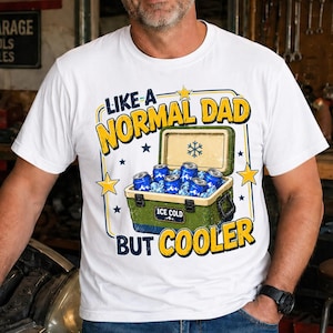 Peut inclure: T-shirt blanc avec l'inscription "LIKE A NORMAL DAD BUT COOLER" en jaune et bleu. Le motif comprend une glacière verte remplie de canettes bleues et de glace. Des étoiles et un flocon de neige sont également présents.