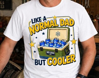 May include: White t-shirt with the text "LIKE A NORMAL DAD BUT COOLER" in yellow and blue. The graphic includes a green cooler filled with blue cans and ice. Stars and a snowflake are also featured.