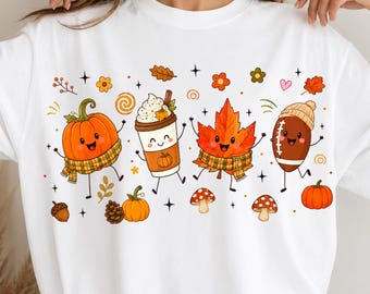 May include: A white crewneck sweatshirt featuring a colorful graphic print of anthropomorphic autumn elements including a pumpkin, a coffee cup, a maple leaf, and a football, all wearing scarves or hats, surrounded by small mushrooms, acorns, and stars.