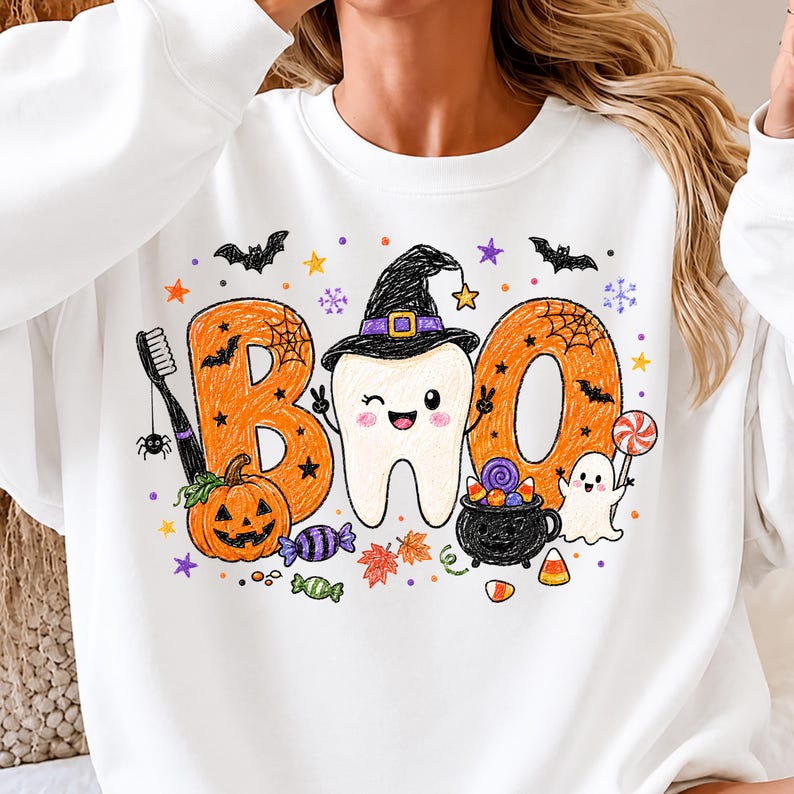K&ouml;nnte beinhalten: Ein wei&szlig;es Sweatshirt mit Rundhalsausschnitt und einer bunten Grafik des Wortes BOO, in dessen Mitte ein Zahn mit Hexenhut abgebildet ist. Das Design zeigt einen K&uuml;rbis, eine Zahnb&uuml;rste, einen Kessel, ein Gespenst, S&uuml;&szlig;igkeiten, Flederm&auml;use und Sterne.