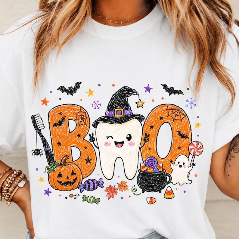 K&ouml;nnte beinhalten: Ein wei&szlig;es T-Shirt mit einem Grafikdruck des Wortes BOO in Orange, mit einem zwinkernden Zahn in der Mitte, der einen schwarzen Hexenhut tr&auml;gt. Das Design umfasst eine Zahnb&uuml;rste, einen K&uuml;rbis, einen schwarzen Kessel, ein Gespenst und Halloween-Symbole.