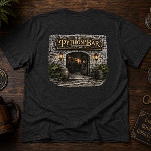 Può includere: Una t-shirt grigio antracite scuro con la grafica dell'ingresso di una taverna in pietra e la scritta The Python Bar Est. 1819. Il disegno include due lanterne, botti di legno e piante verdi che fiancheggiano l'ingresso ad arco in pietra.