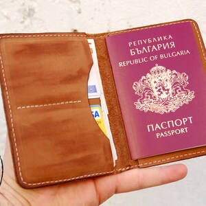 May include: A brown leather passport holder with a passport for the Republic of Bulgaria inside. The passport is red with a gold emblem and the words "PASSPORT" in both Bulgarian and English.