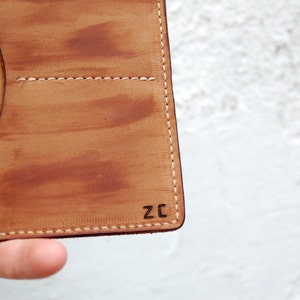 May include: A brown leather wallet with a stitched edge and the initials "ZC" embossed on the bottom right corner.