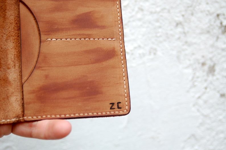 May include: A brown leather wallet with a stitched edge and the initials "ZC" embossed on the bottom right corner.