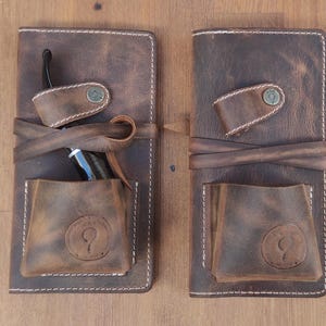 May include: Two brown leather pouches with white stitching. Each pouch has a flap with a snap closure and a small pocket on the front. One pouch has a pipe inside.