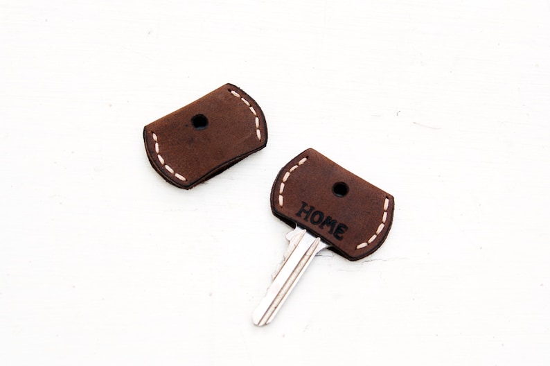 May include: Two brown leather key covers with white stitching. One cover has the word "HOME" printed on it.