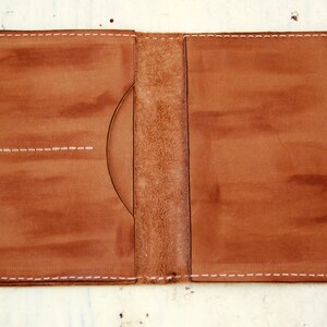 May include: A brown leather passport holder with white stitching. The holder has two pockets on the left side and one on the right.
